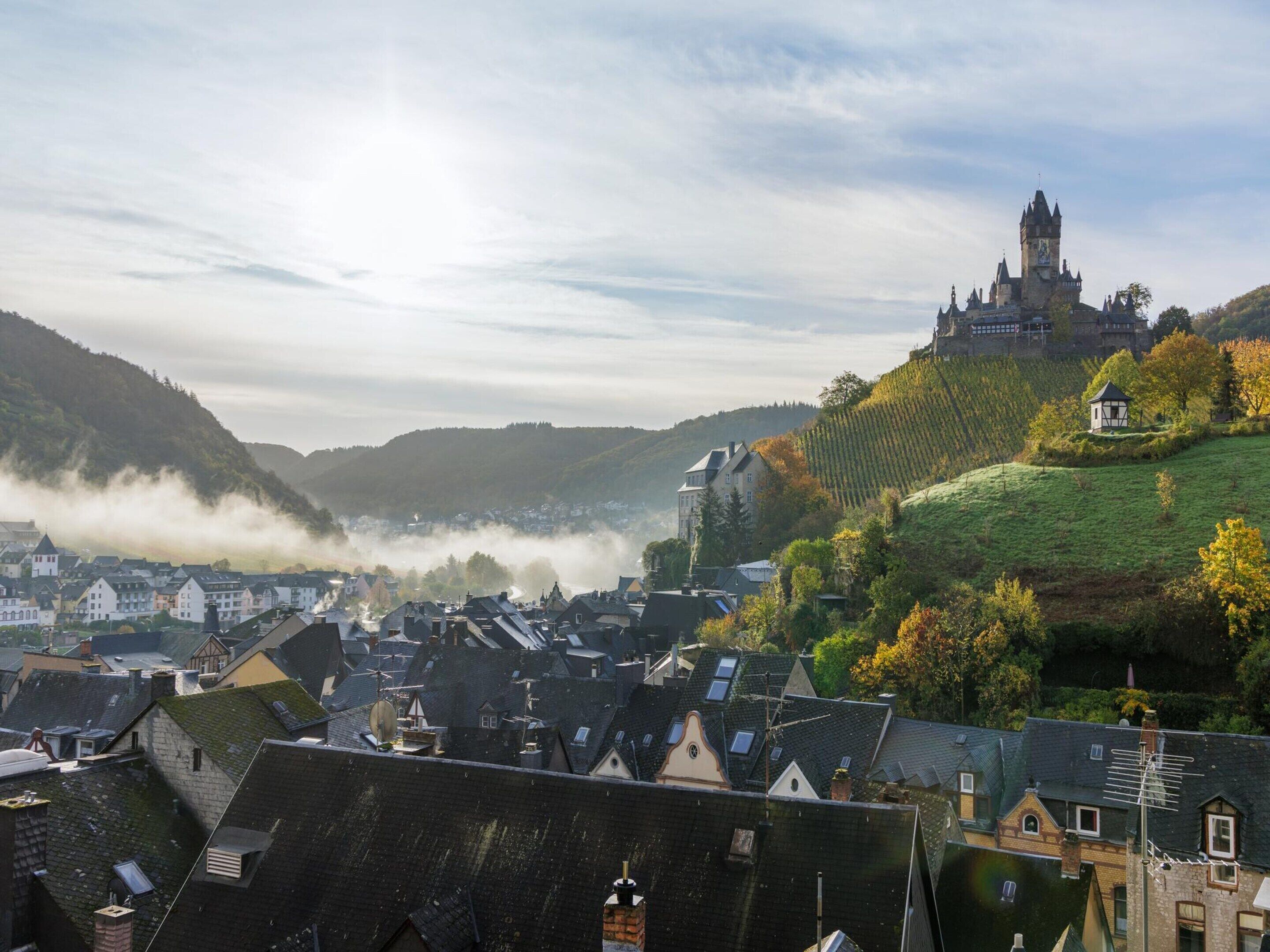 A town with historic buildings, a prominent castle on a hill, and a valley with mist.