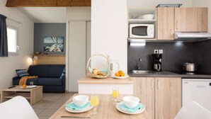 A compact living space with a kitchenette, a dining area with breakfast setup, a sofa, and a painting on the wall. - Modern Family Getaway (Le Chateau-d'Oleron)