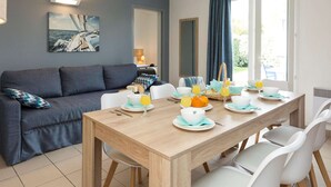 A dining area with a wooden table set for breakfast, a grey sofa, and a painting of a sailboat on the wall. - Modern Family Getaway (Le Chateau-d'Oleron)