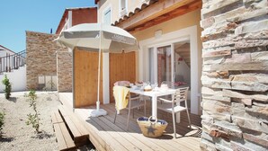 Eine Holzterrasse mit Gartenmöbeln, einer Steinmauer und einem überdachten Sitzbereich mit Sonnenschirm.