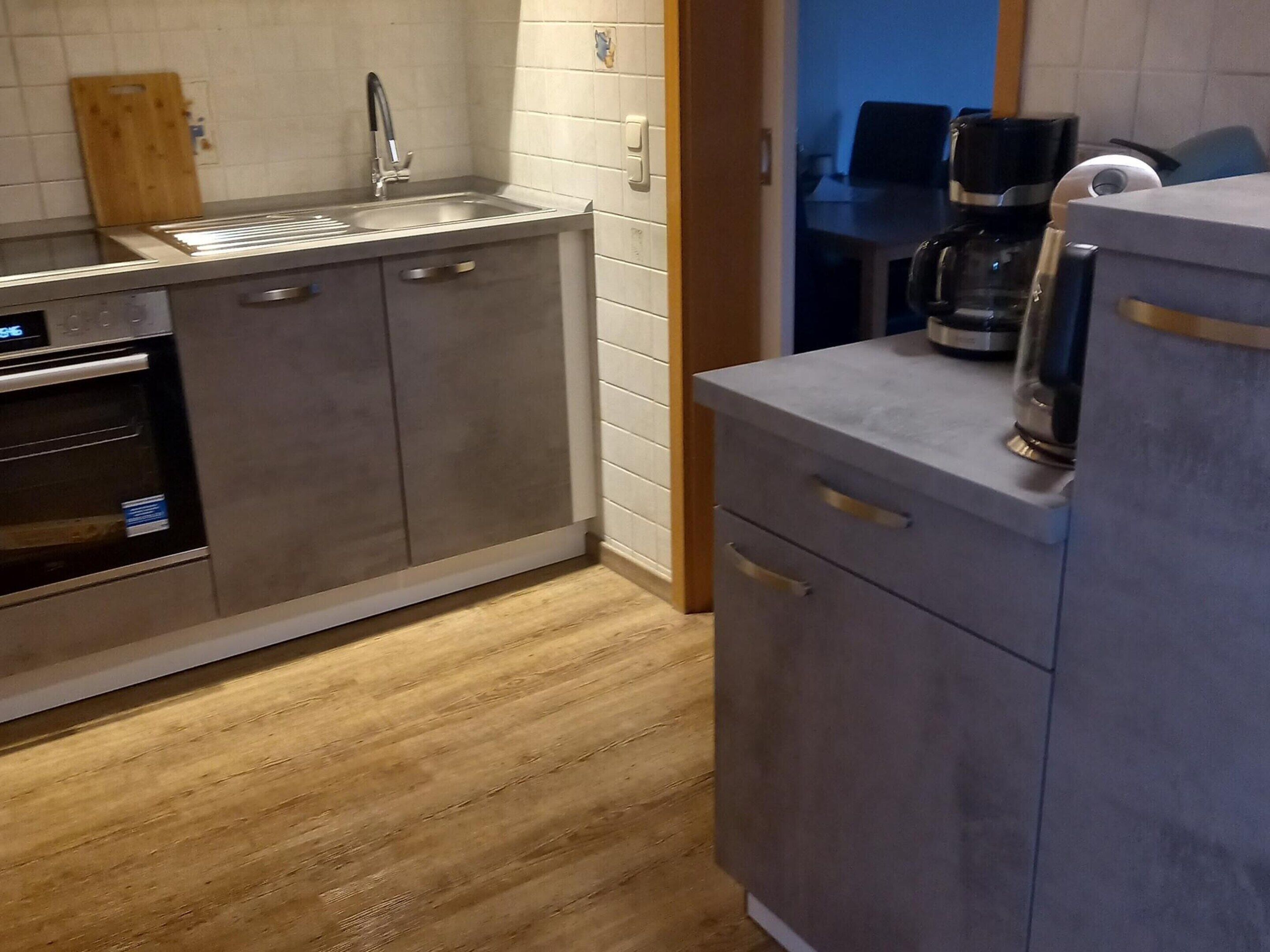 Una cocina moderna con electrodomésticos de acero inoxidable, piso de madera y un armario gris.