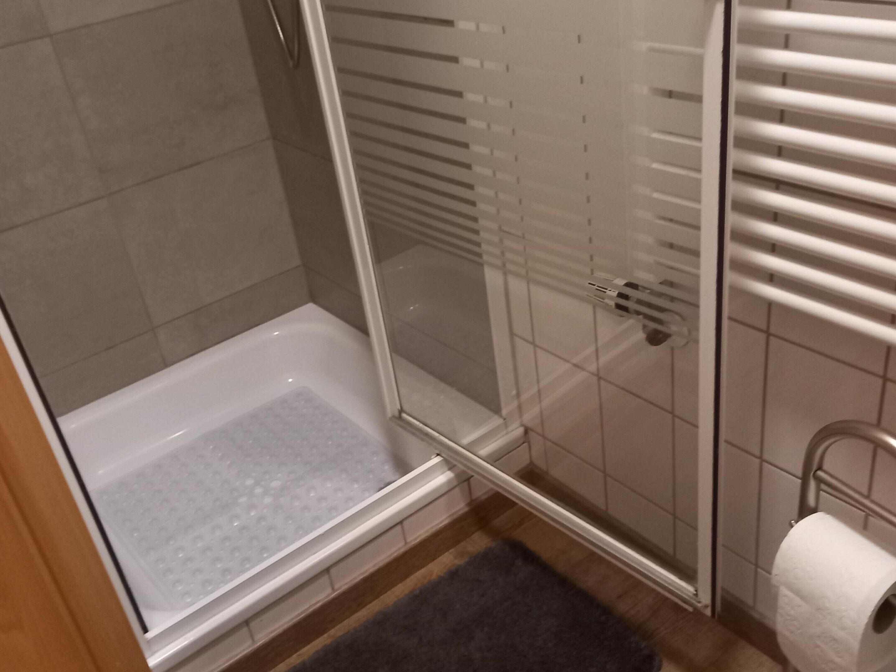 A shower with a glass door, a white bathtub, and a towel rack with a roll of toilet paper.