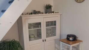 A white cabinet with glass doors, a small table with a radio, and a potted plant. - Chic Apartment in Stormbruch near Ski Area (Diemelsee)