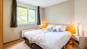 A bedroom with a bed, bedside tables, a window with curtains, and a radiator.