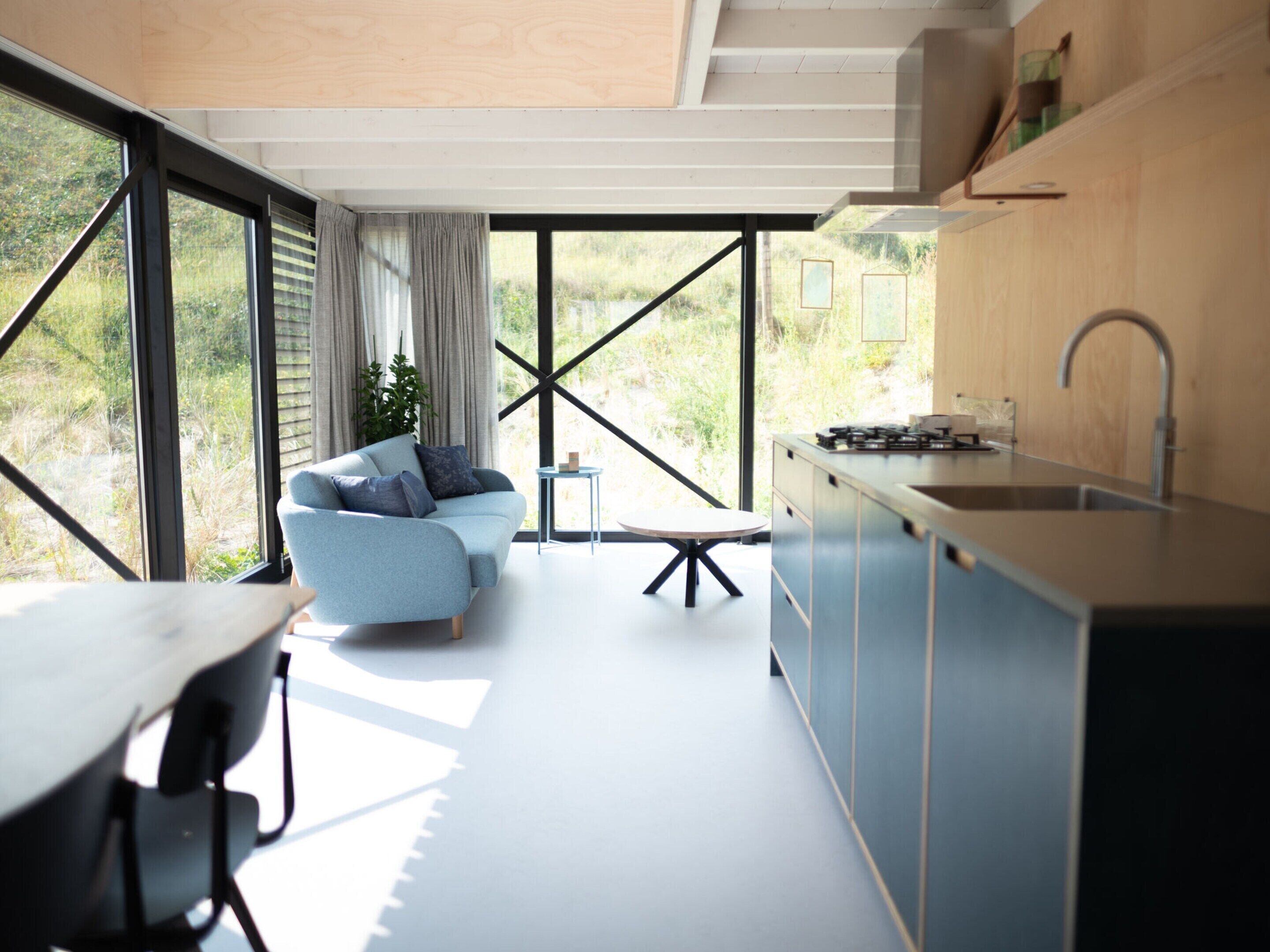 A modern kitchen with a dining area, large windows, and a view of greenery.