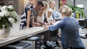 Een receptiebalie met een receptionist, een groep mensen en een kamerplant.