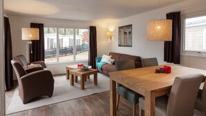 Een moderne woonkamer met een houten eettafel, banken en een groot raam met gordijnen.