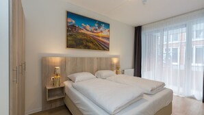 A modern hotel room with a large bed, a nightstand, a painting of a sunset, and a large window with curtains. - Apartment in Zoutelande Near the Beach (Zoutelande)