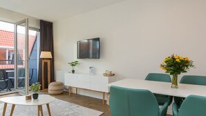 A modern, well-lit room with a white dining table, teal chairs, a white cabinet, a flat-screen TV, and a potted plant. - Apartment in Zoutelande Near the Beach (Zoutelande)
