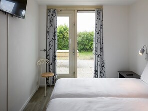 A bedroom with a bed, a chair, a nightstand, a TV, and a view of the outdoors. - Villa in Zeeland With Sauna & Beach Access (Kamperland)