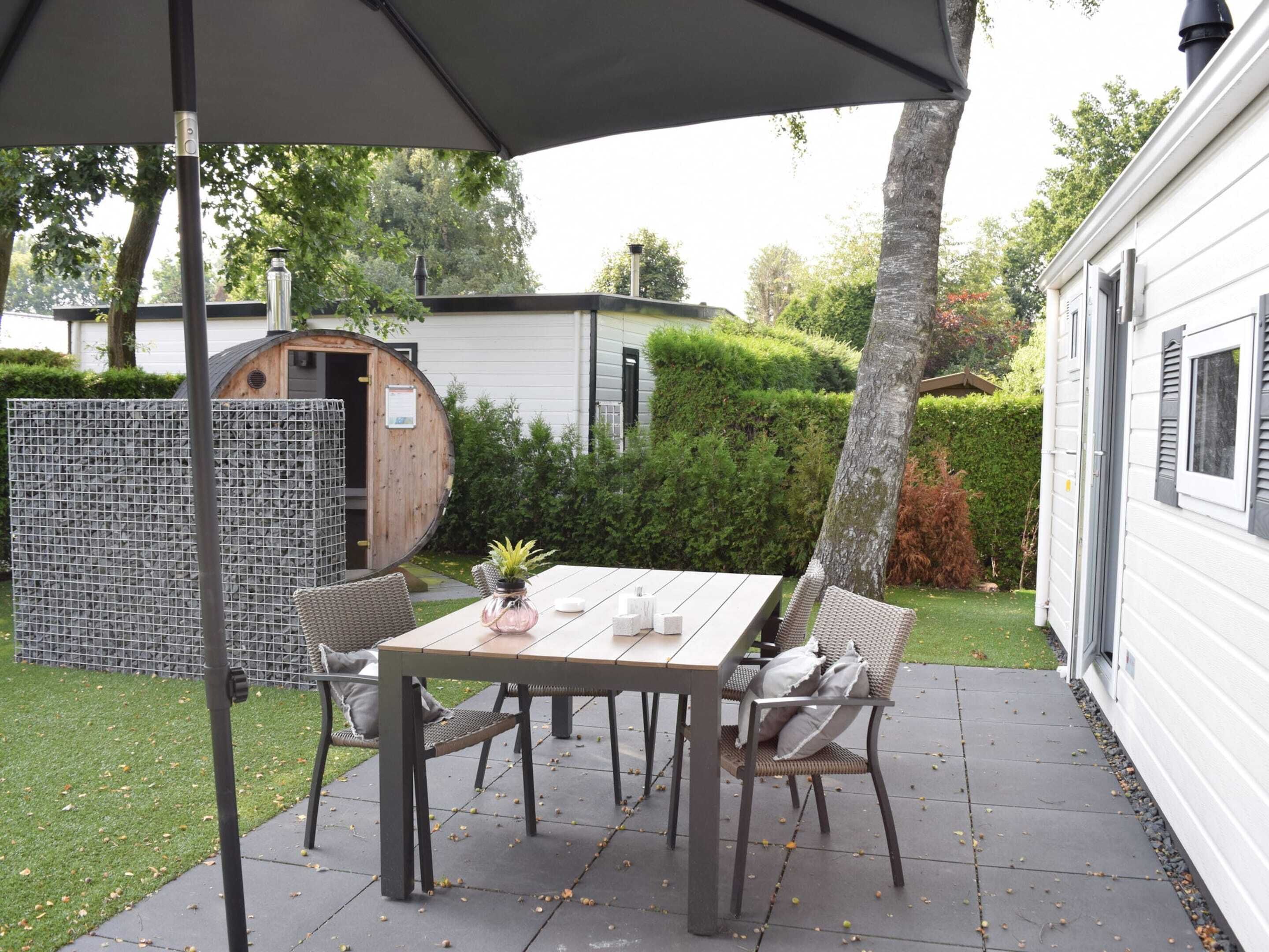 A patio with a table and chairs, a wooden barrel, and a white building in the background.