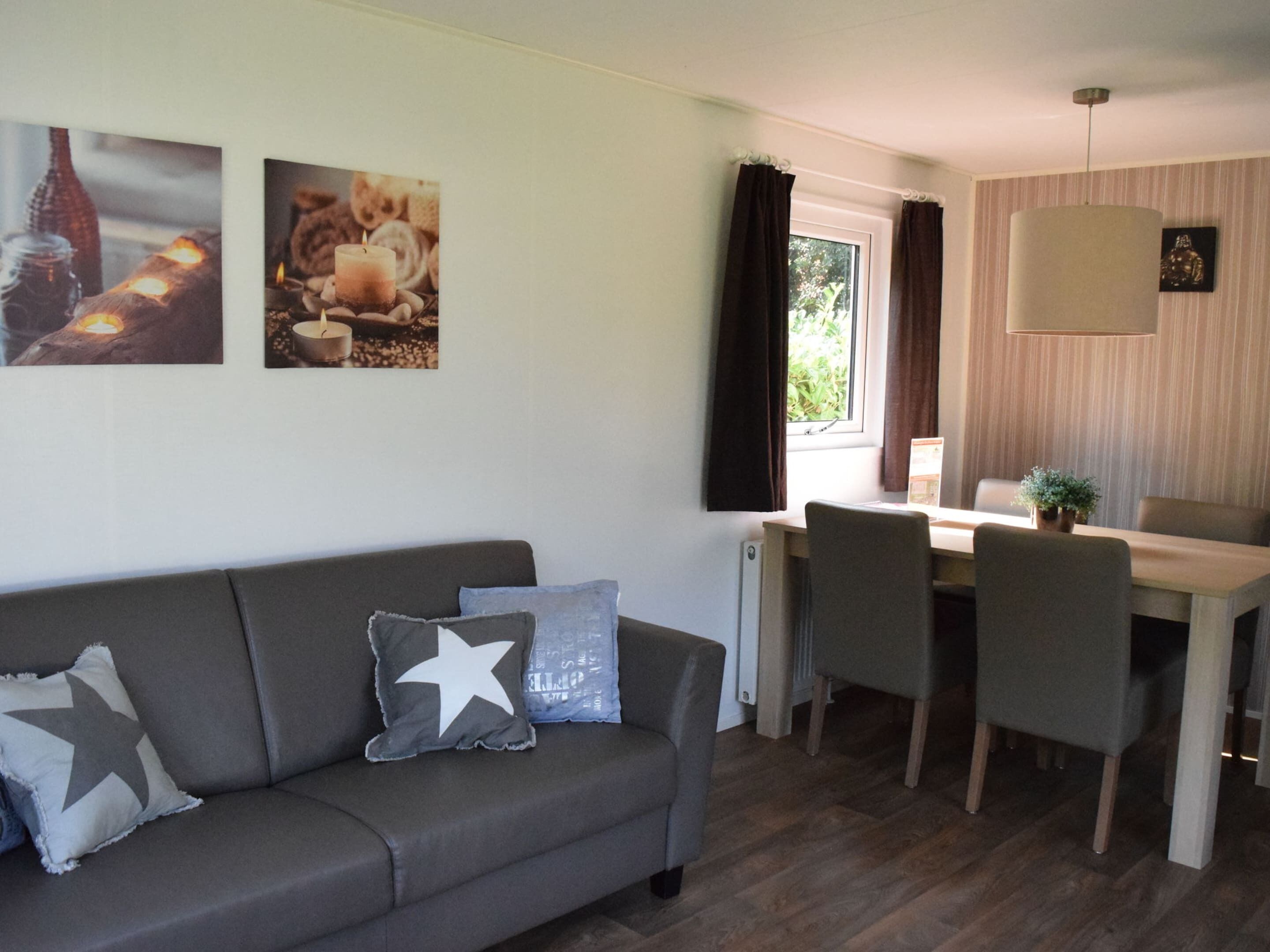 A modern living room with a grey sofa, a dining table with chairs, and a window with curtains.