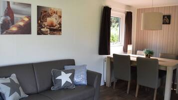 A modern living room with a grey sofa, a dining table with chairs, and a window with curtains.