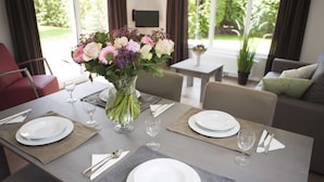 A dining table set with plates, cutlery, and wine glasses, with a vase of flowers in the center. - Wellness Chalet in Nature (Voorthuizen)