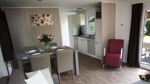 A modern living room with a sofa, dining table, and chairs. There is a kitchen area with cabinets and a red chair. - Wellness Chalet in Nature (Voorthuizen)