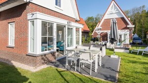Ein zweigeschossiges Haus mit Ziegelverkleidung, großen Fenstern und einer Terrasse mit Gartenmöbeln.