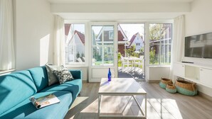 Ein helles Wohnzimmer mit einem türkisblauen Sofa, einem Couchtisch und einem Fernseher auf einer weißen Kommode.