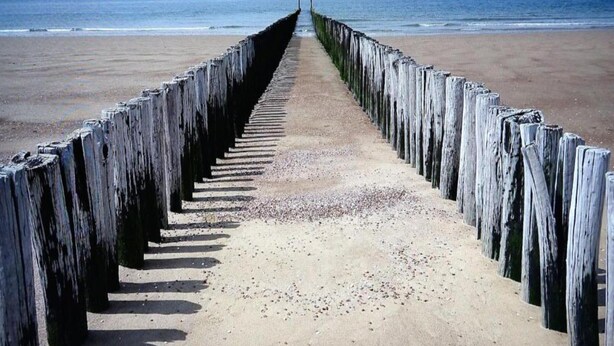 Ein Strand mit einer Holzpromenade, die zum Meer führt.