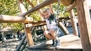 Un enfant qui grimpe sur une structure de jeu en bois, munie de chaînes.
