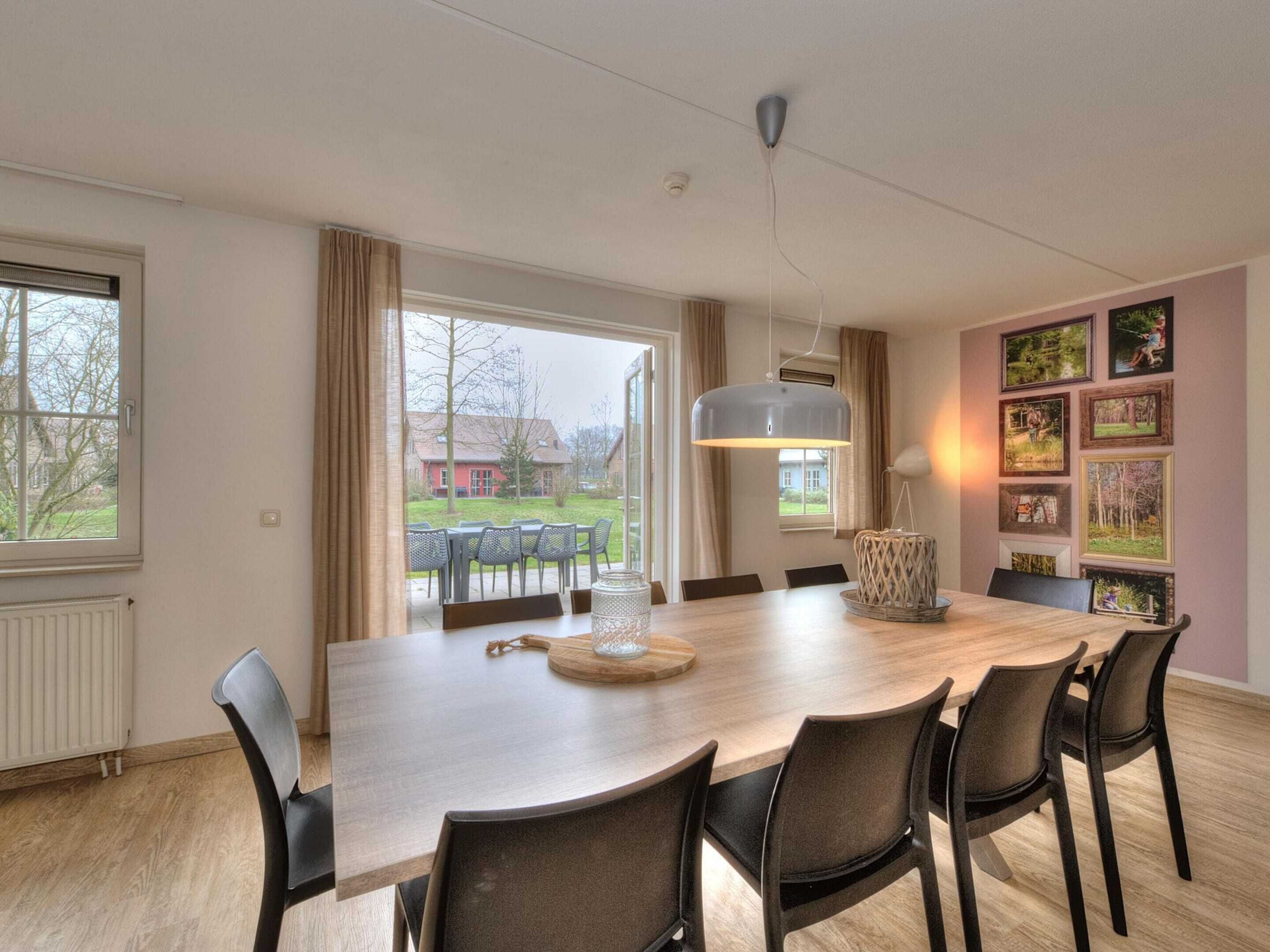 A dining area with a large wooden table, black chairs, and a hanging light fixture.