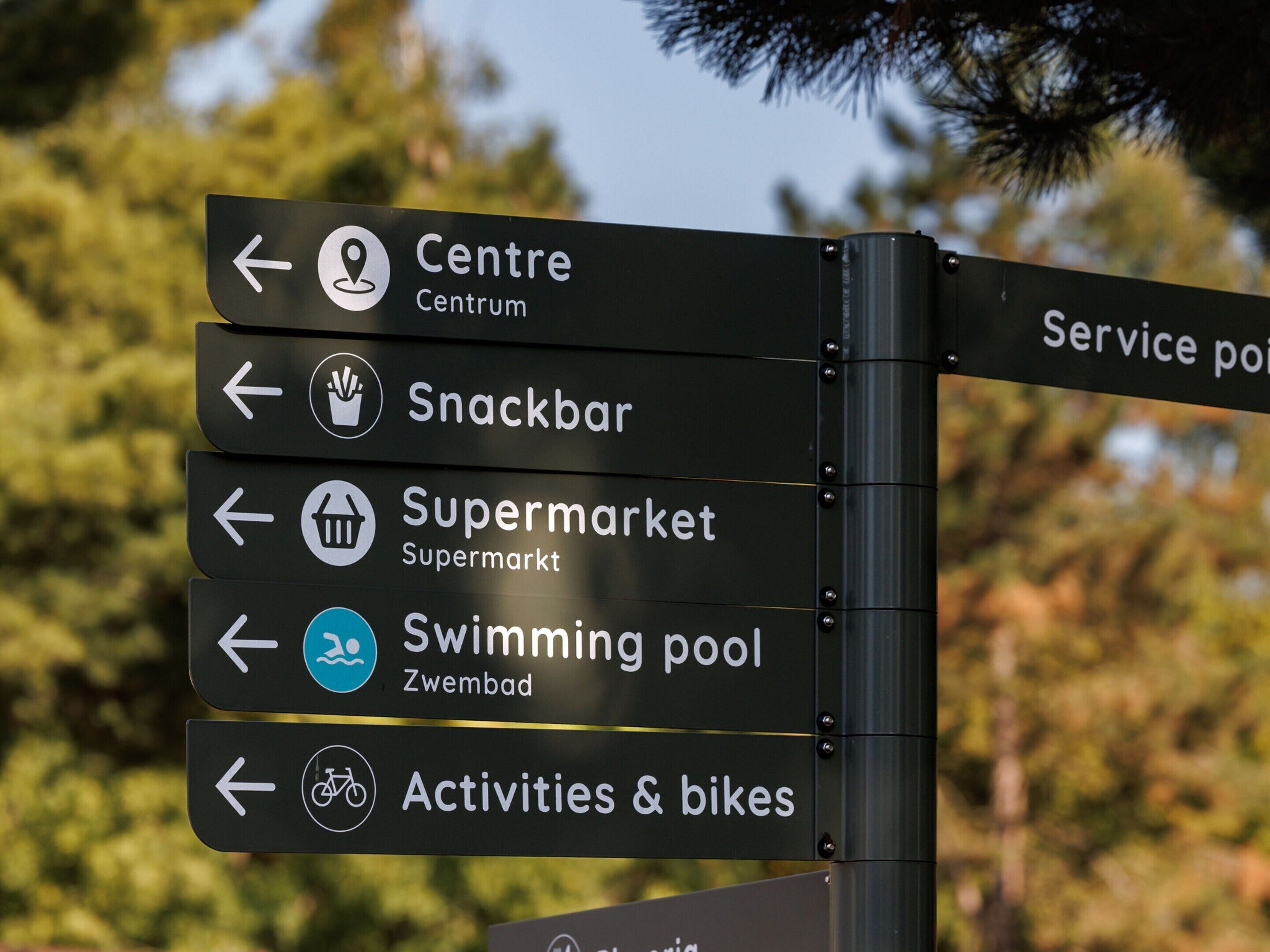 A directional sign with multiple arrows pointing to various amenities such as Centre, Snackbar, Supermarket, Swimming pool, and Activities & bikes.