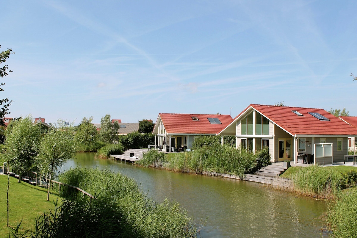 A riverside property with a red-roofed house, a dock, and a grassy area.