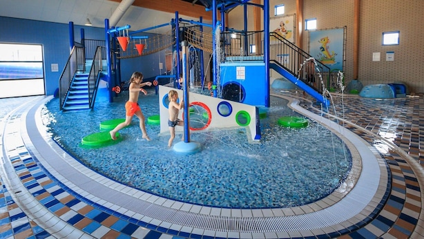 An indoor water play area with slides, climbing structures, and a pool.