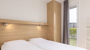 Cama doble con sábanas blancas en una habitación con cabecera de madera y ventana con cortinas.