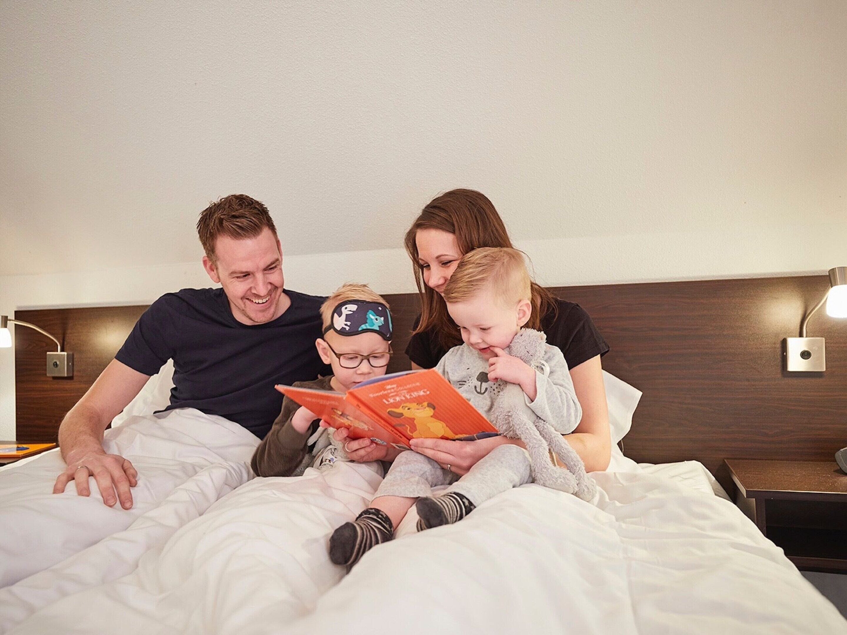 Una familia de tres sentada en una cama en una habitación de hotel, leyendo un libro juntos.