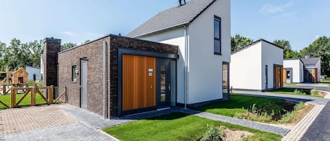 A modern residential building with a brick facade, a wooden door, and a well-maintained lawn.