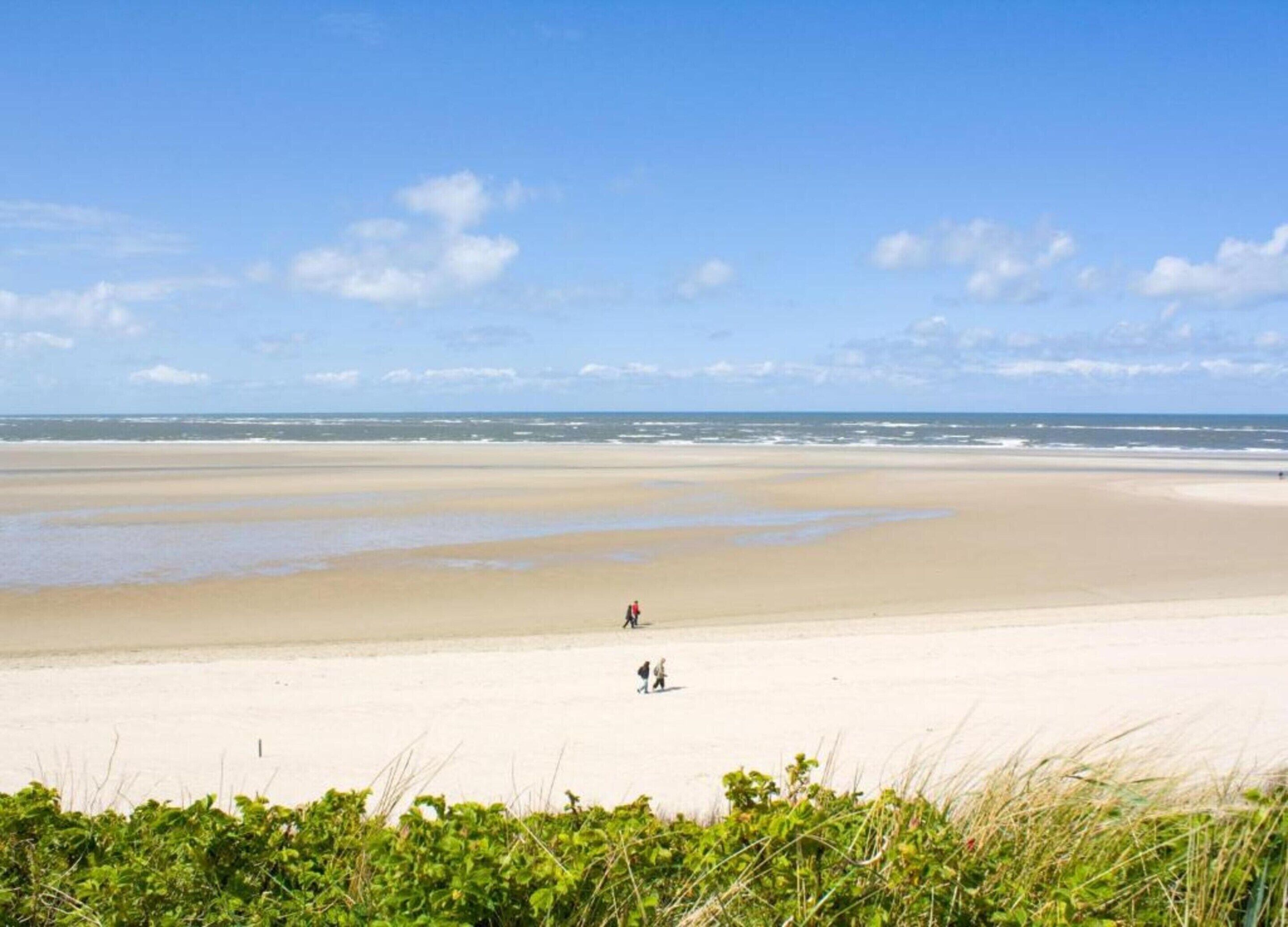 A wide sandy beach with a clear sky and a few people walking.