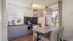 A modern kitchen with a dining area, featuring a large window, a built-in oven, and a coffee machine. - Restyled Villa With Dishwasher, Near the Beach (Kamperland)