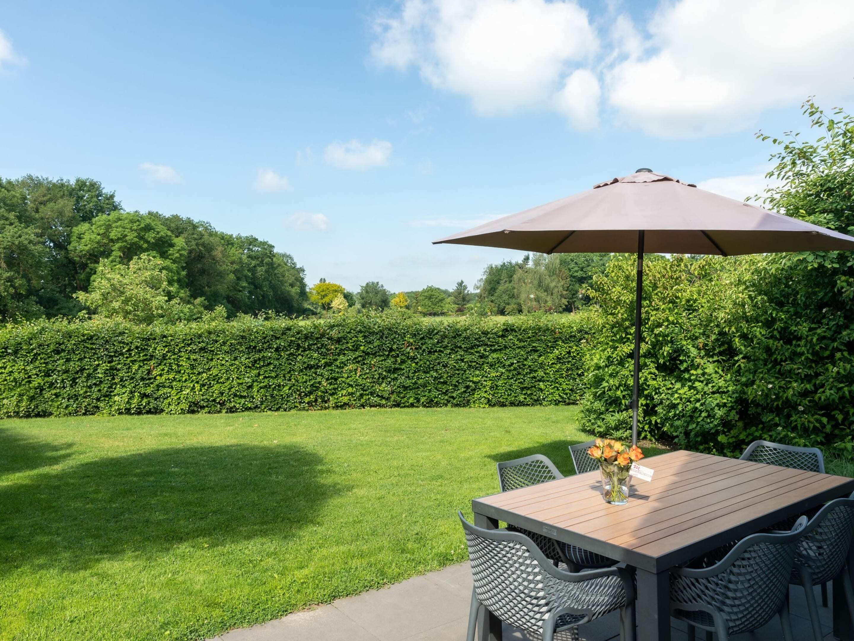 An outdoor patio with a table and chairs, a large umbrella, and a well-maintained lawn.