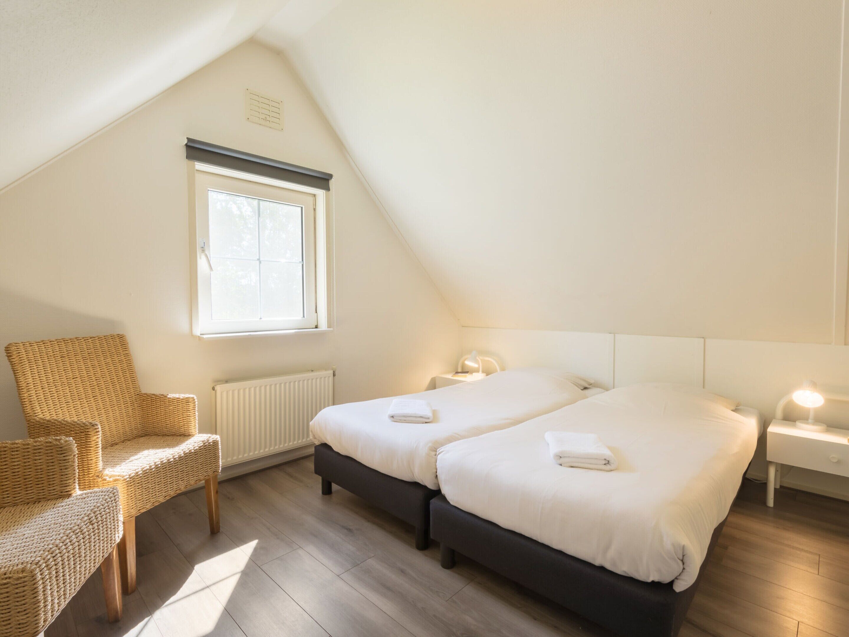 A bedroom with two beds, a chair, and a window.