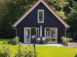 Una casa de color oscuro con techo rojo, puertas de vidrio grandes y un pequeño patio con mobiliario exterior.