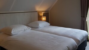 A hotel room with two beds, a nightstand with a lamp, and a window with curtains. - Modern Villa With Garden (Almen)