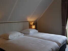 Una habitación de hotel con dos camas, una mesita de noche con lámpara y una ventana con cortinas.