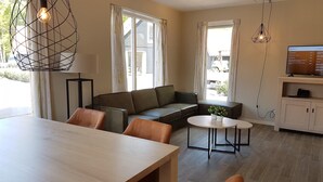 A modern living room with a wooden dining table, leather sofas, a small round table, and a TV on a wooden cabinet. - Modern Villa With Garden (Almen)