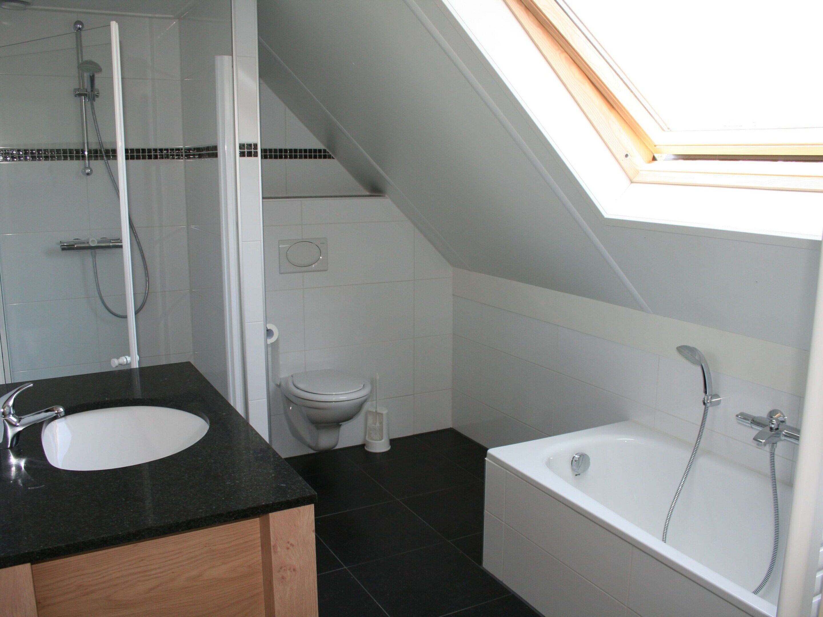 A modern bathroom with a skylight, a bathtub, a toilet, and a sink.