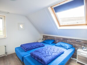 Ein Schlafzimmer mit zwei Betten, einem Oberlicht, einer Heizung und einem weißen Nachttisch.