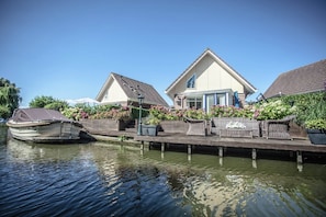 A canal-side property with a dock, a rowboat, and a wooden deck with outdoor furniture. - Lovely Holiday Home With Jetty Near Ijsselmeer (Medemblik)