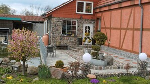 Una casa con facciata in pietra, tetto rosso e un giardino con diverse piante e uno stagno.