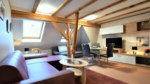 Un moderno loft con soffitto alto, travi a vista in legno, un'accogliente area salotto con divano e poltrone, un tavolo da pranzo e una zona cucina con TV e pensili.