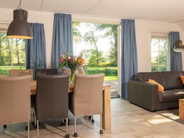 Una sala de estar moderna con comedor, que incluye un sofá, sillas, una mesa y un jarrón con flores.