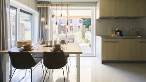 A modern kitchen with wooden cabinets, a dining area with a table and chairs, and a view of a garden through large windows. - Lodge in Vlissingen Near North Sea Beach (Vlissingen)