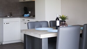 Uma cozinha moderna com armários brancos, forno embutido e máquina de café. Há uma mesa de jantar com quatro cadeiras e uma garrafa de vinho sobre ela.
