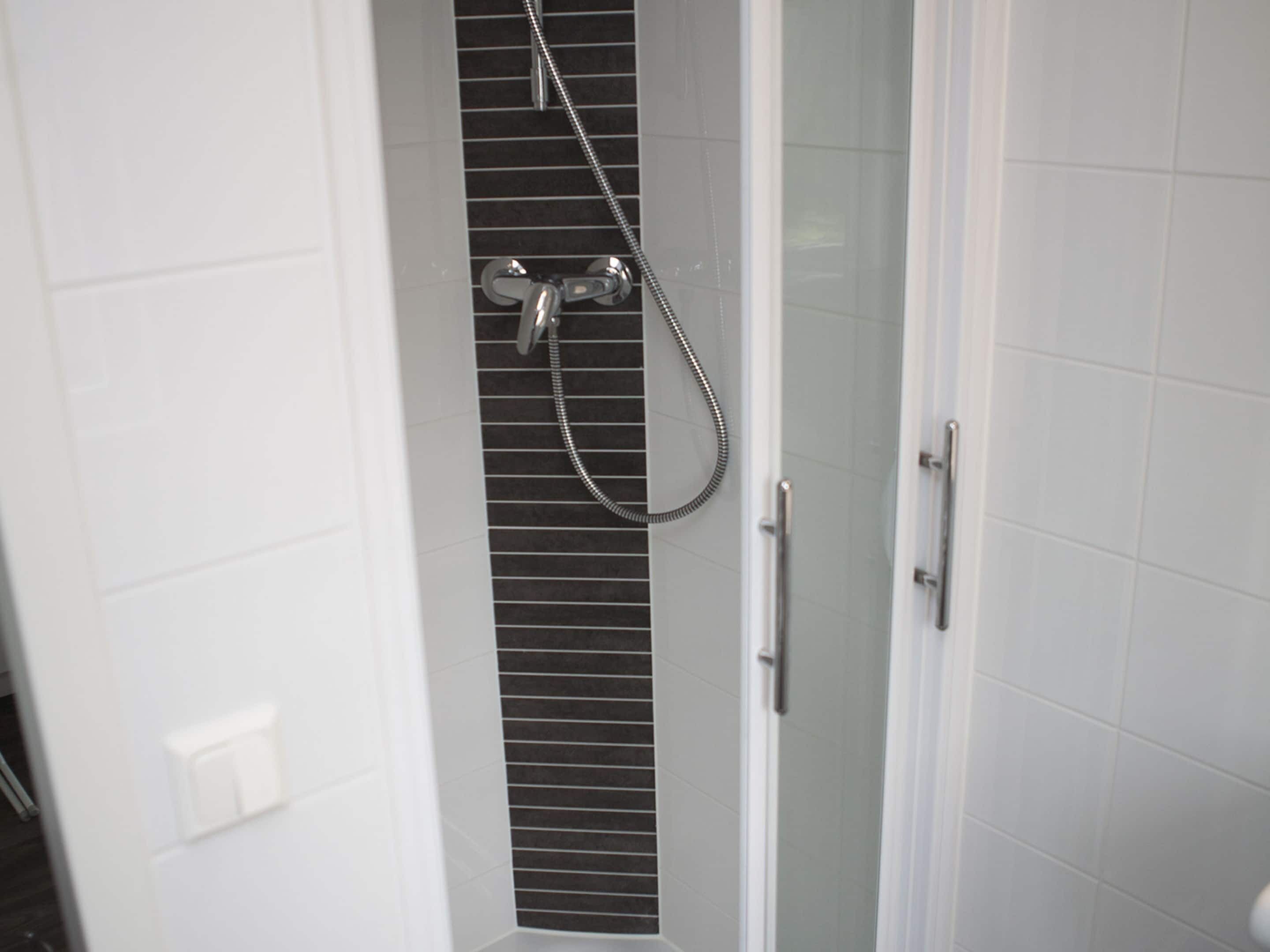 A bathroom with a shower, white tiled walls, and a vented shower enclosure.