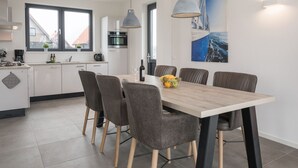 A modern kitchen with white cabinets, a dining table with six chairs, and a large window. - Luxury Villa on the Water (Ossenzijl)