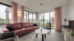 A modern living room with a red sofa, a round coffee table, and large windows with curtains. - Luxury Villa on the Water (Ossenzijl)