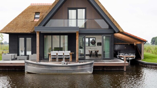 A modern house with a thatched roof, large windows, and a dock with a boat. - Luxury Villa on the Water (Ossenzijl)
